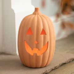 Ceramic jack-o'-lantern with a smiling face, glowing warmly from within, placed on a wooden surface.