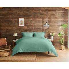 Inviting bedroom with grey bedding on a wooden bed, against a rustic wood-paneled wall. Decor includes a woven chair, plants, and soft lighting.
