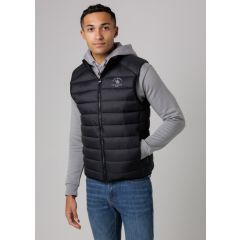 Young man in a black puffer vest over a gray hoodie and blue jeans, standing with a hand in pocket, looking confidently at the camera.