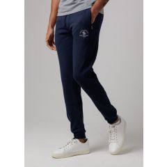 Man wearing navy joggers with embroidered logo, paired with a gray shirt and white sneakers. Casual, relaxed style on a neutral background.