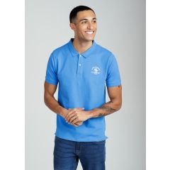 Smiling man in a blue polo shirt and blue jeans, standing against a gray background. He has tattoos on his arm and appears upbeat and casual.