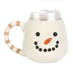 Front view of ceramic snowman face mug with carrot nose and striped handle including soft socks