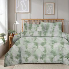 A bedroom with a wooden bed featuring green and white fern-patterned bedding, a small plant on a side table, and abstract wall art.