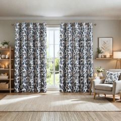 Cozy living room with floral-patterned blue and beige curtains framing a bright window. A beige armchair, lit candles, and plants create a calming ambiance.