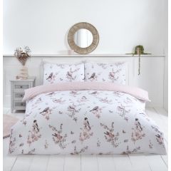 A neatly made bed with floral and bird-patterned bedding, a round mirror above, a small bedside table with decor, and a plant on the ledge.