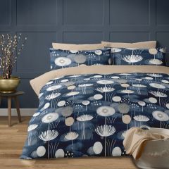 A cozy bedroom with a watter garden floral-patterned navy duvet on a beige bed, set against a dark paneled wall. A side table holds a pot with decorative branches, and a basket with a blanket adds warmth.