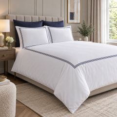 White duvet cover set with elegant navy embroidered border detailing, styled on a bed in a modern luxury bedroom